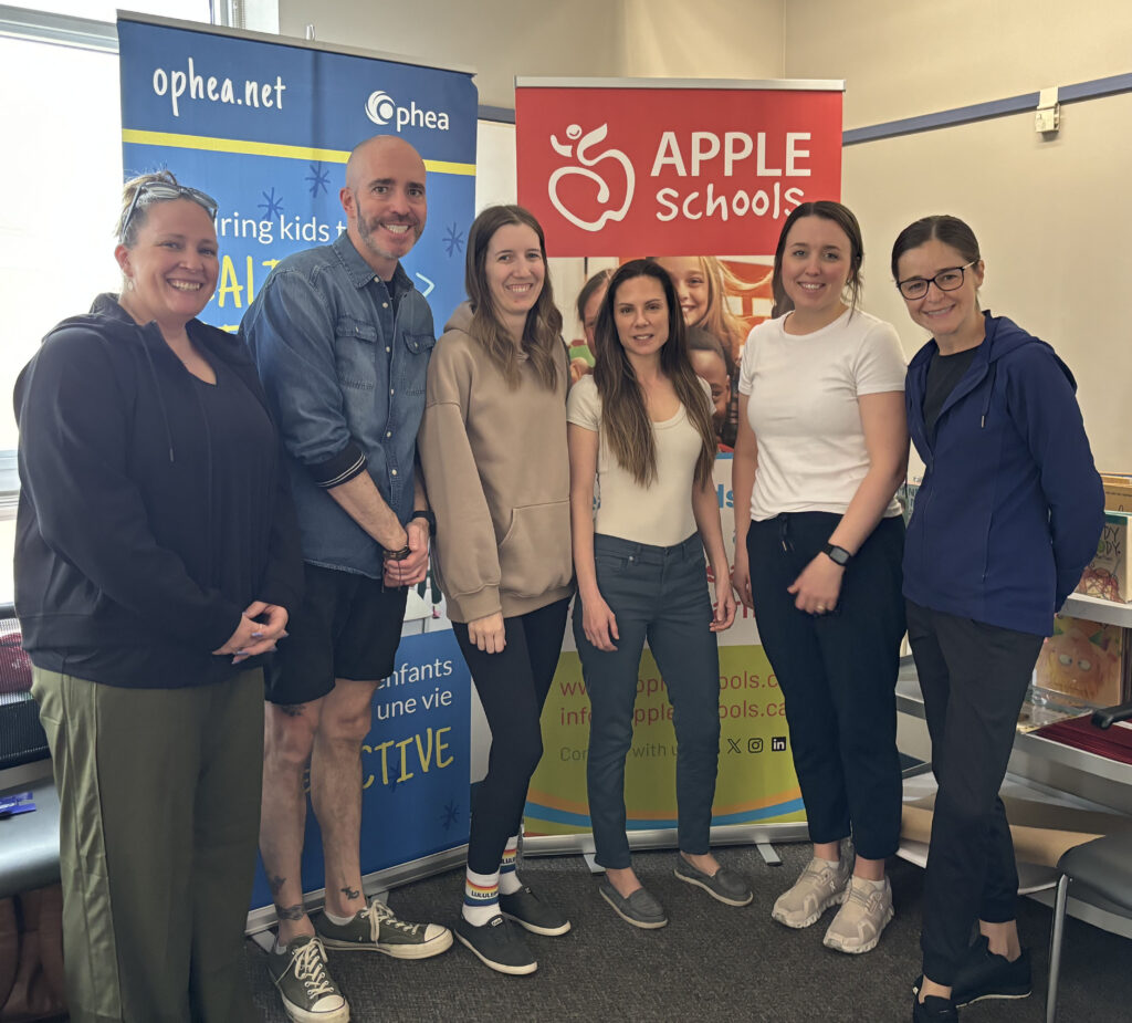 Team of school health champions stand smiling in front of an APPLE Schools and Ophea sign